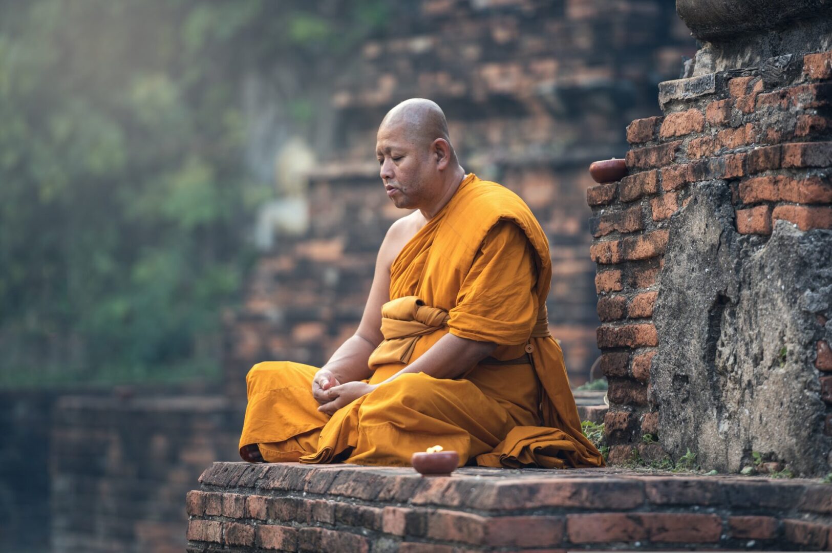 A monk sitting on the ground in front of a brick wall.