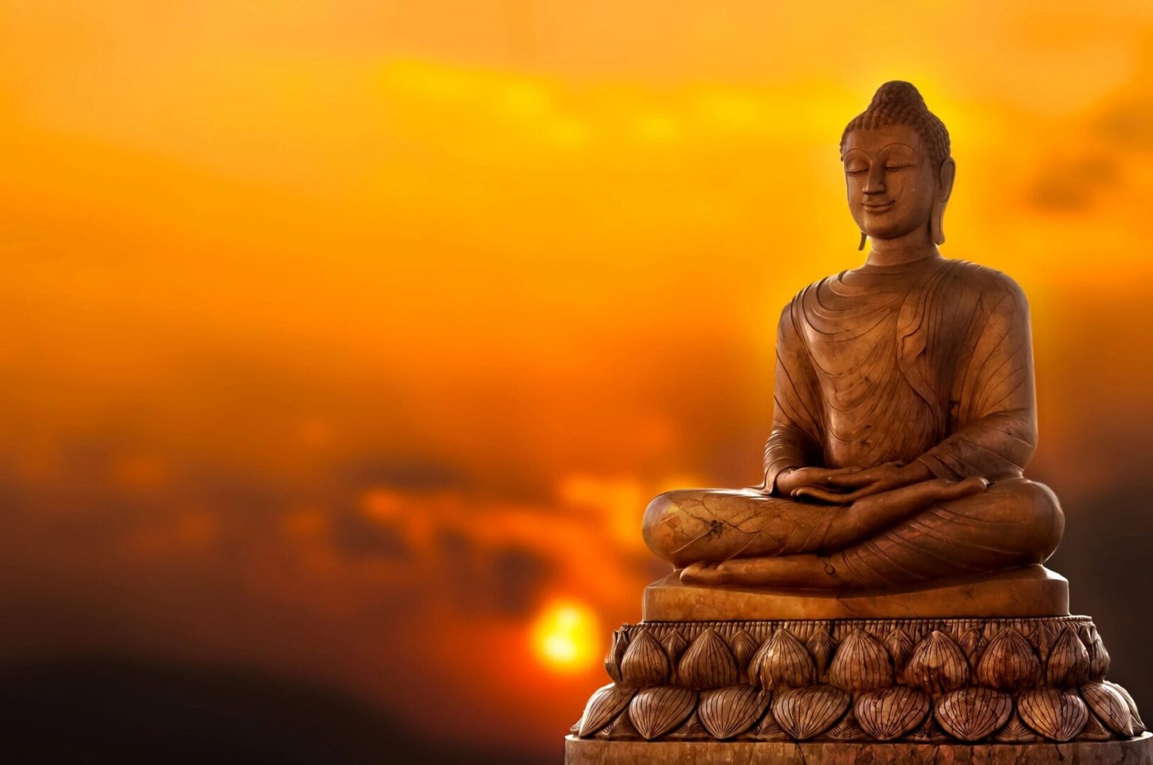 A statue of buddha sitting in front of the setting sun.