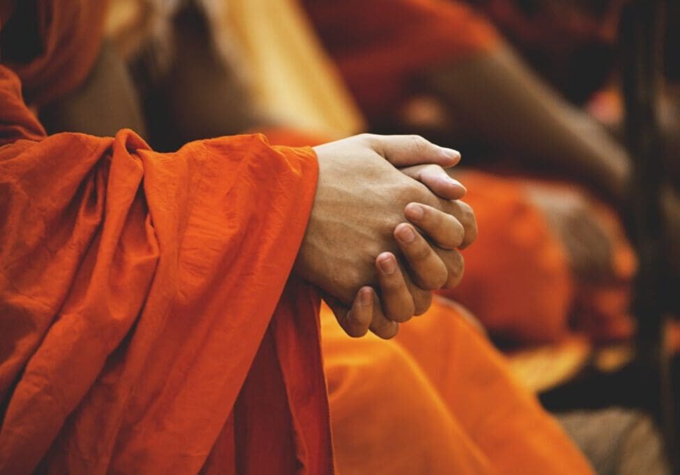 A person in orange robes holding their hands together.