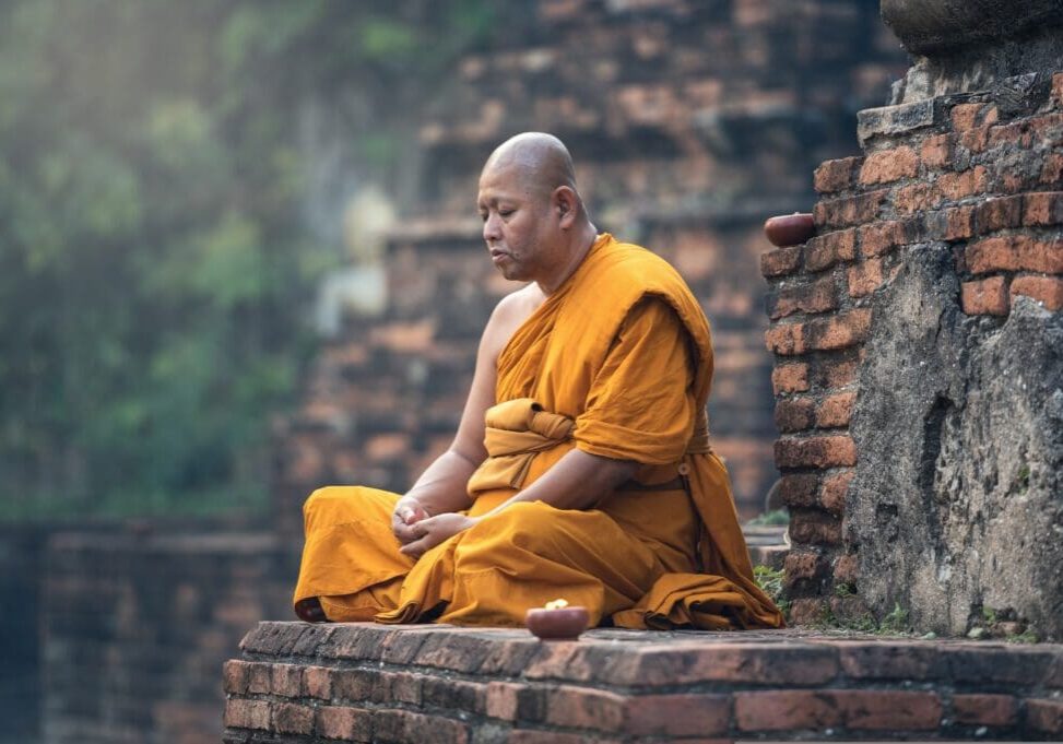 A monk sitting on the ground in front of a brick wall.