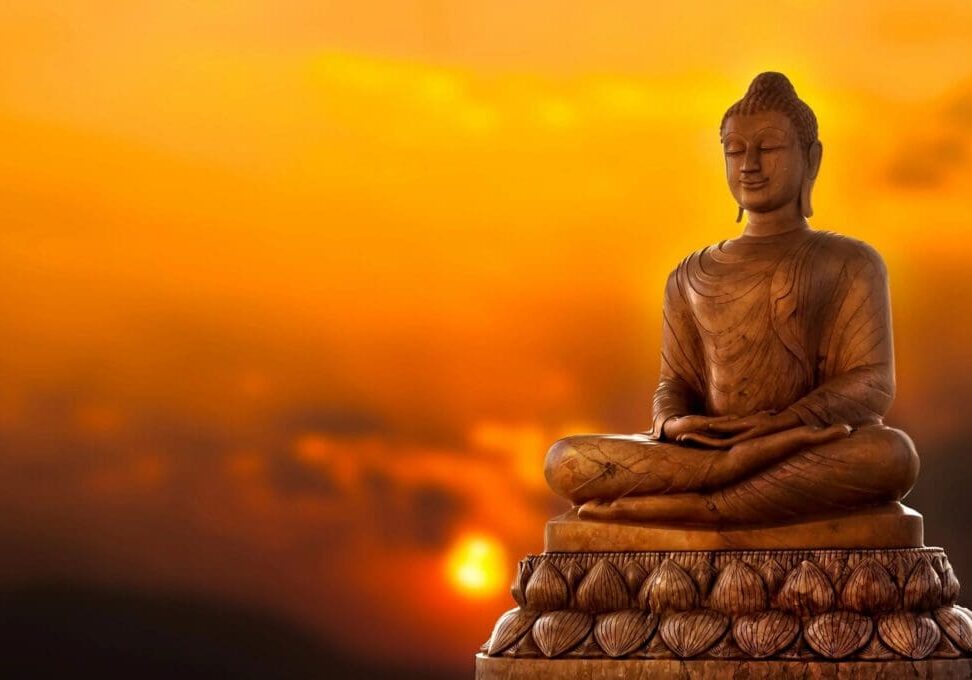 A statue of buddha sitting in front of the setting sun.